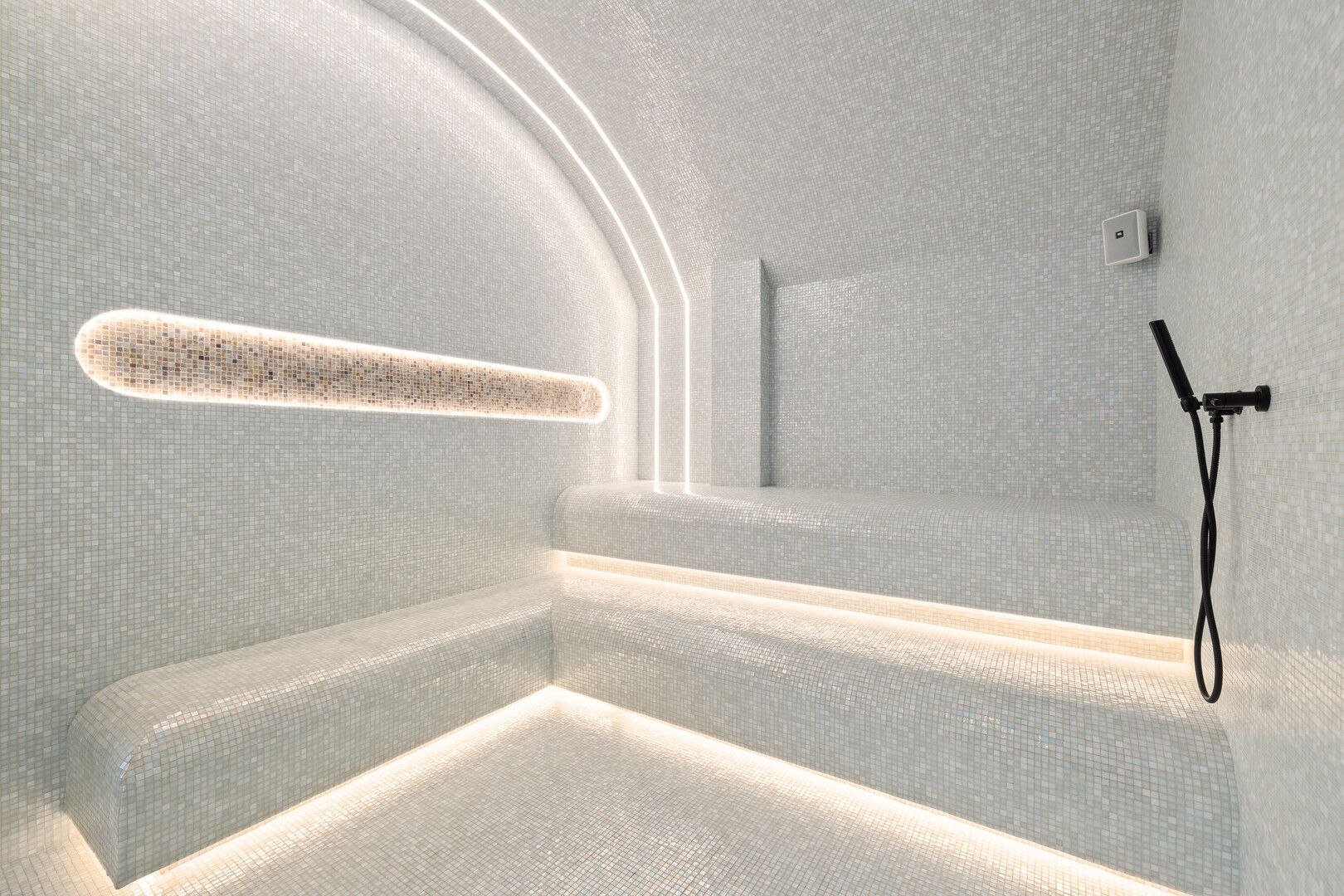 Mosaic-tiled steam room with sculpted benches and linear LED lighting