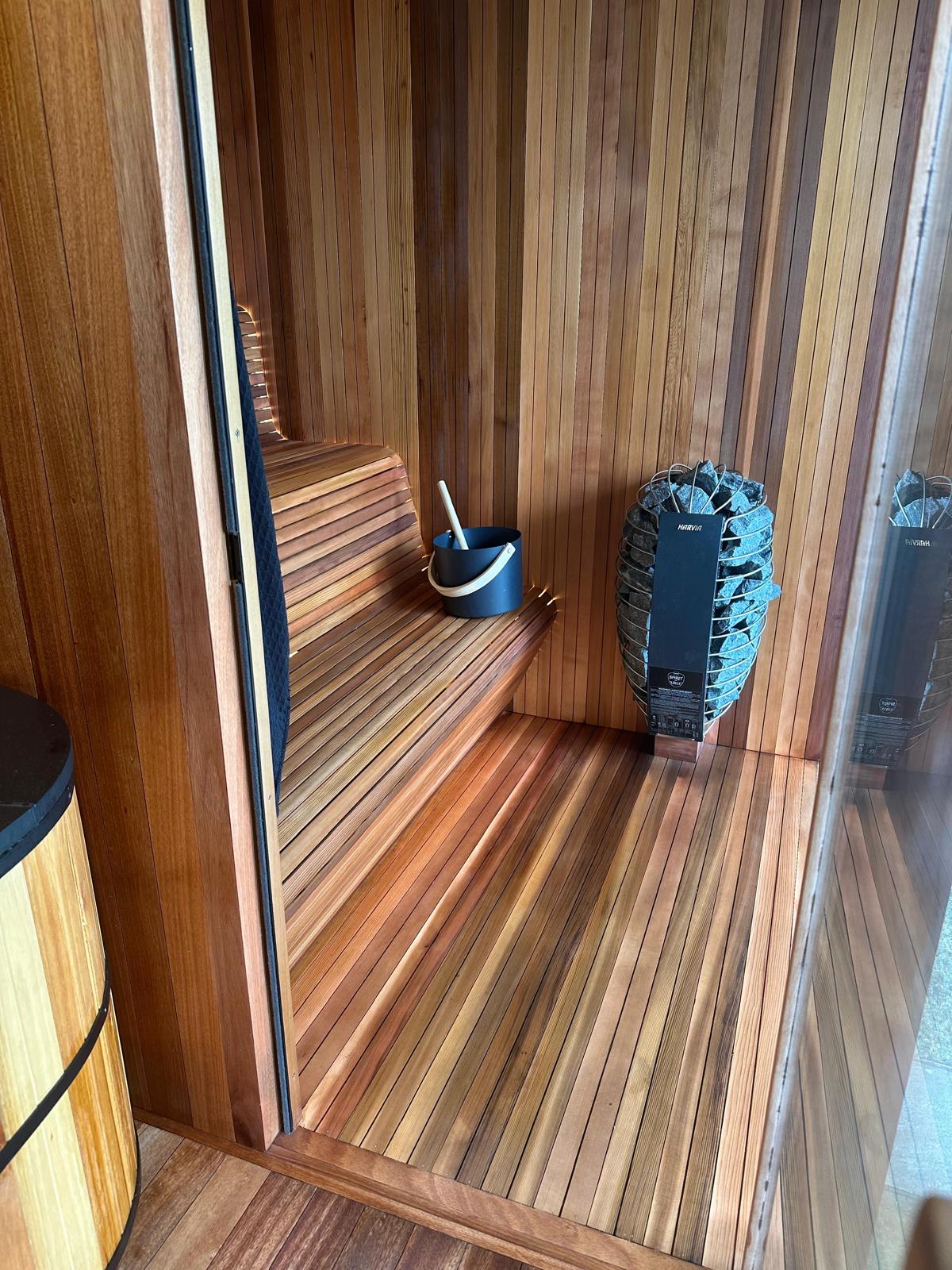 Sauna interior through glass door — clear cedar and Harvia heater