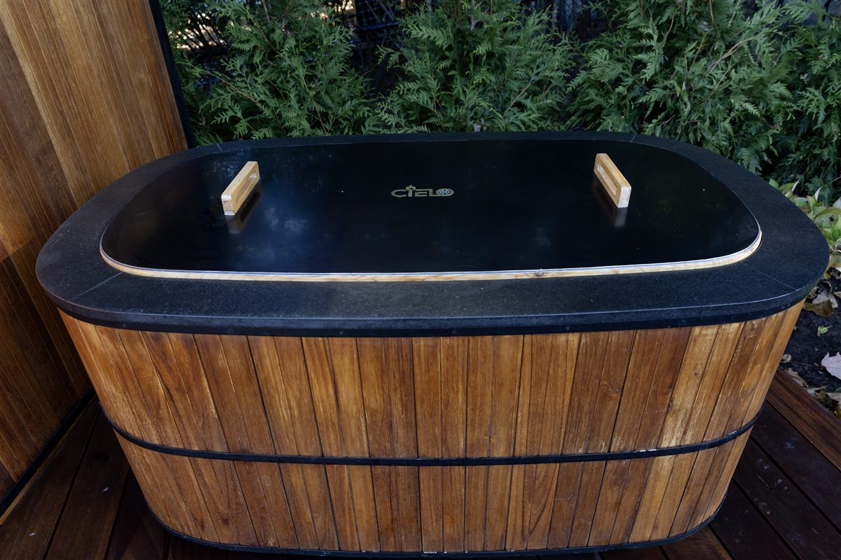 Teak-wrapped cold plunge with an engraved lid on an outdoor deck